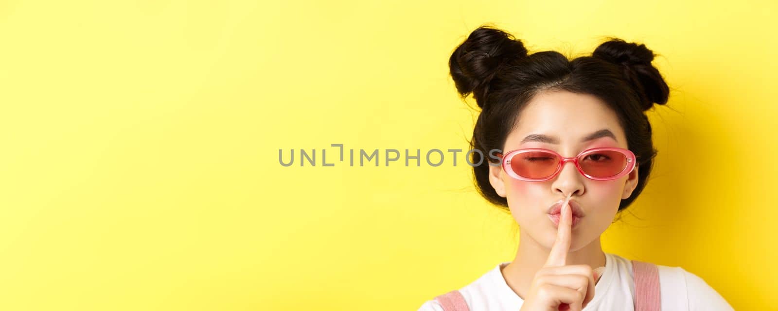 Summer fashion concept. Close-up portrait of glamour asian woman in sunglasses telling a secret, asking be quiet, making hush taboo sign and winking at camera.
