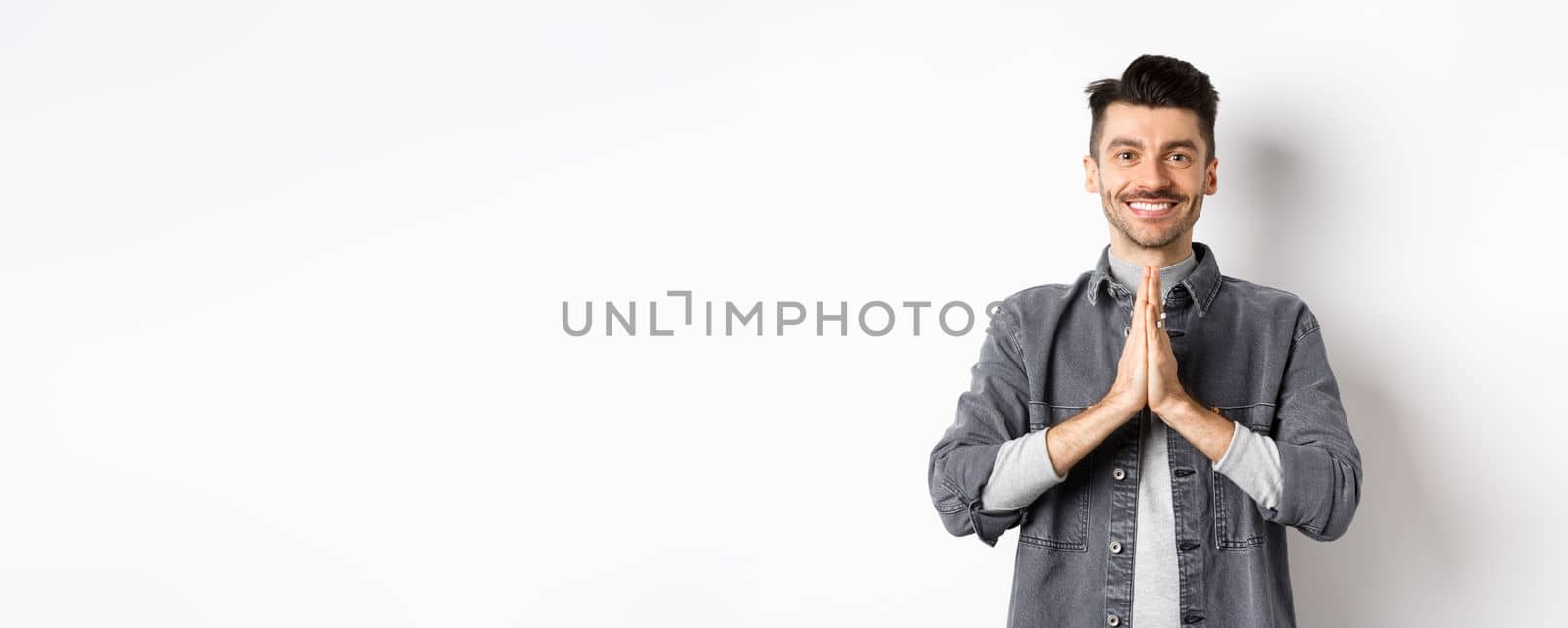 Thank you. Smiling friendly guy showing namaste gesture in gratitude, grateful for help, standing happy on white background by Benzoix