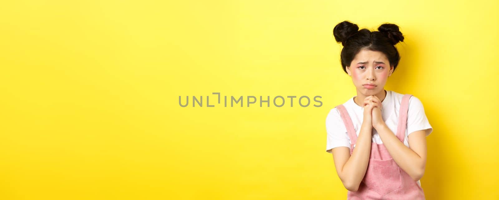 Sad asian girl pleading for help, begging you, sulking and whining, standing on yellow background by Benzoix