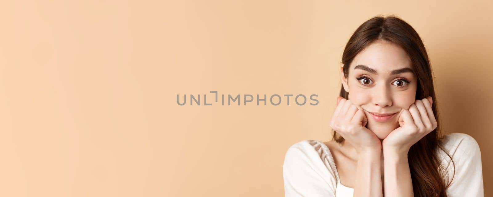 Portrait of intrigued girl listening with interest and excitement, hear interesting story, smiling amused, standing on beige background by Benzoix