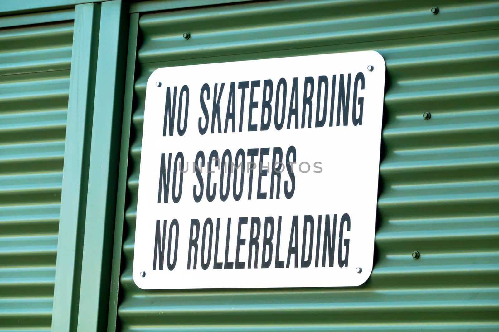 A sign with the text No Skateboarding, No Scooters, No Rollerblading on a metal wall. by oasisamuel