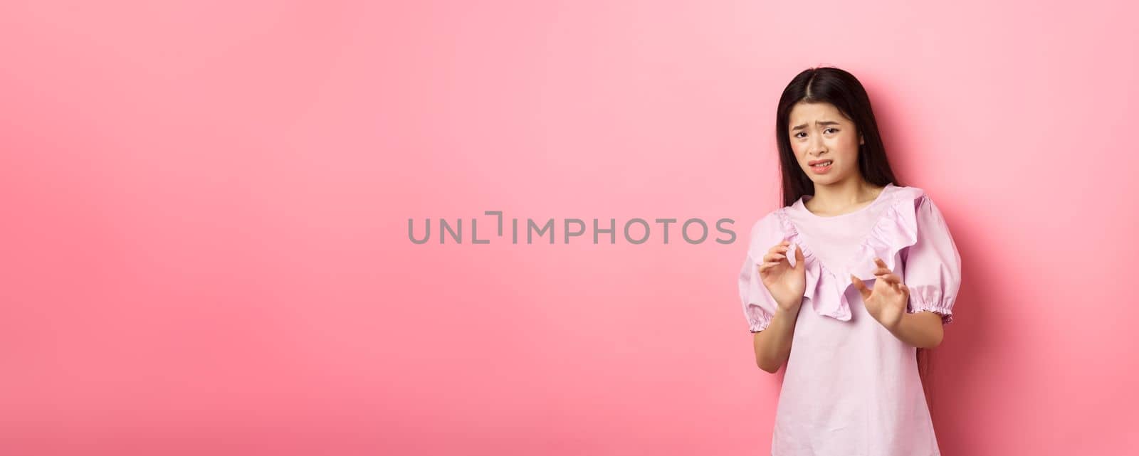 Stay away from me. Disgusted asian girl raising hands to block someone, cringe from aversion, look reluctant and asking to stop, rejecting something bad, pink background by Benzoix