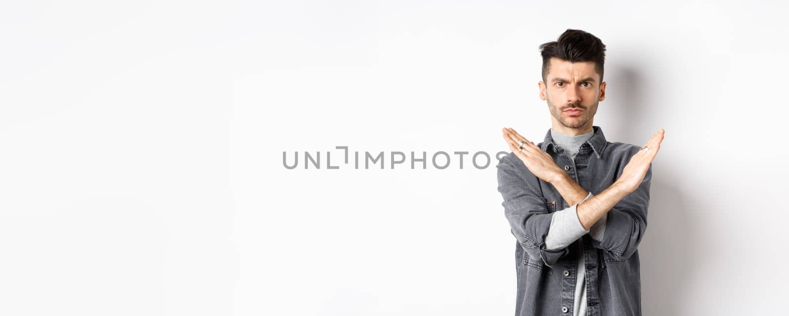Angry man show cross gesture to stop or say no, frowning and looking serious, disagree and prohibit bad situation, standing on white background.