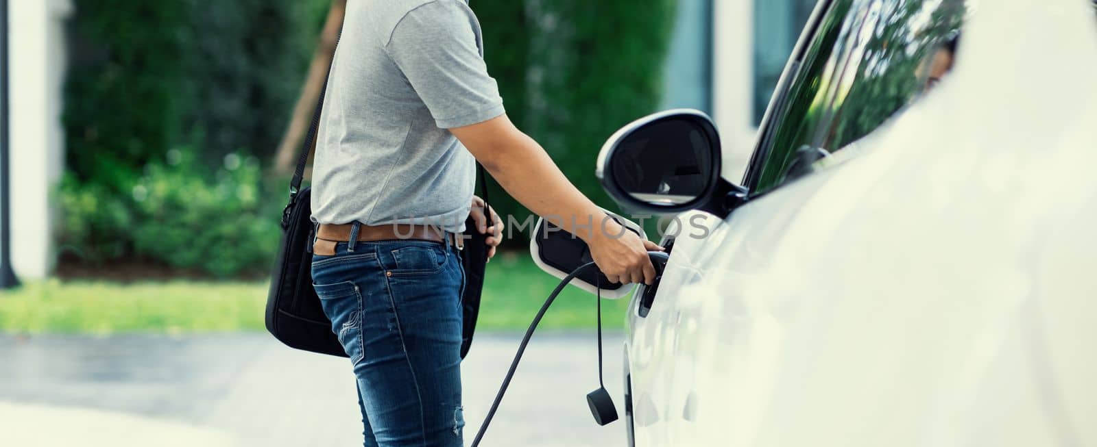 Progressive asian man recharge his EV car at home charging station. by biancoblue