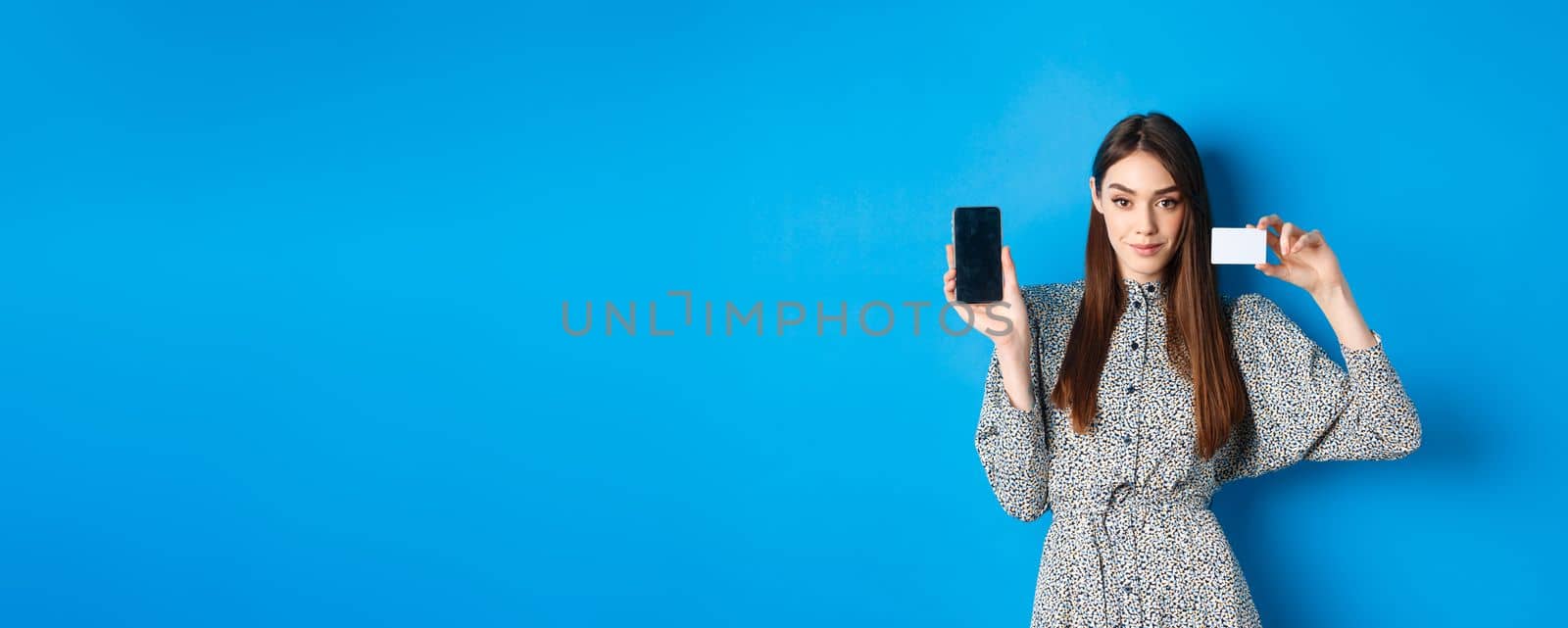 Online shopping. Confident beauty woman showing plastic credit card and empty smartphone screen, showing stop, standing on blue background by Benzoix