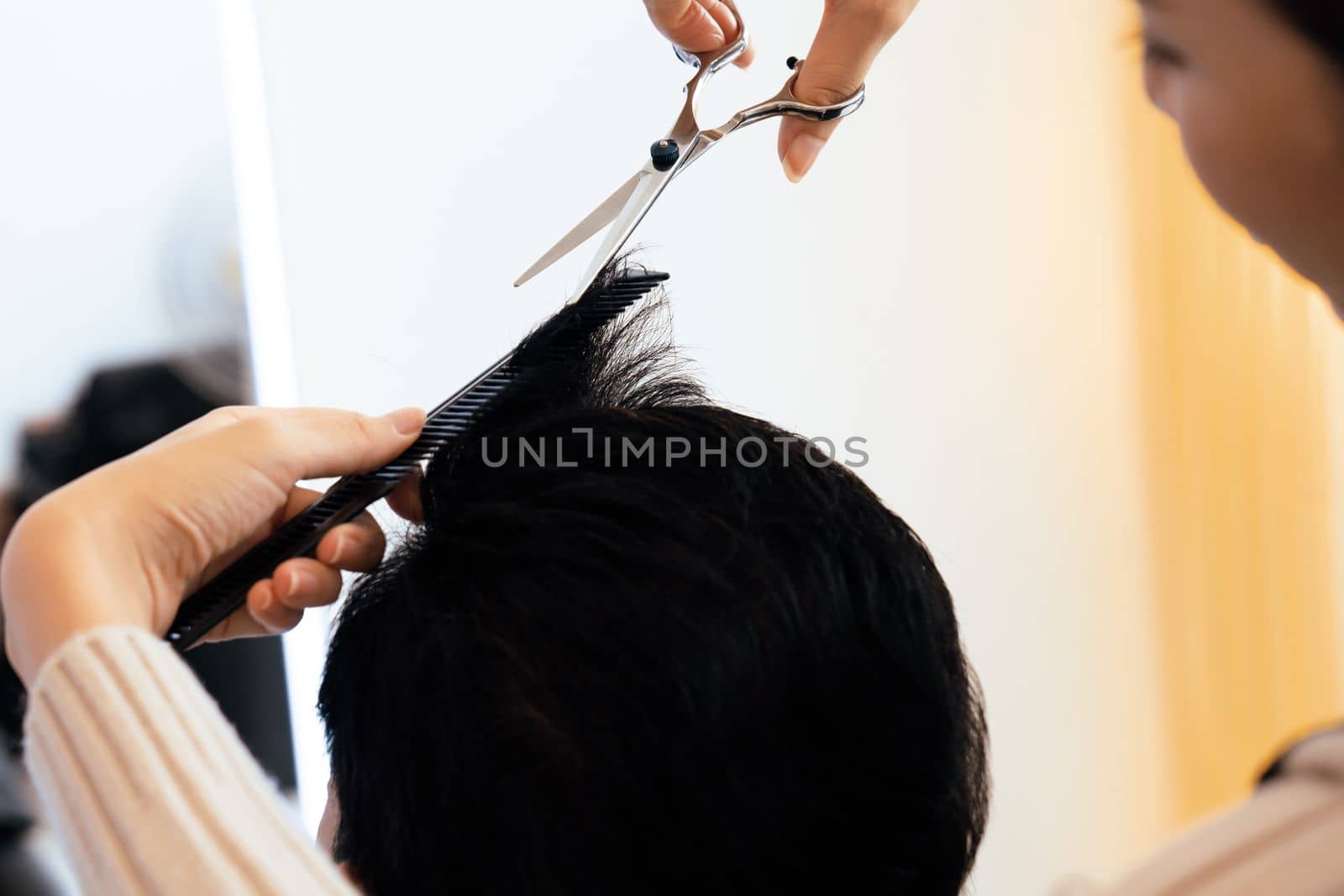 Closeup asian female barber making haircut for male customer with male hairstyle in qualified barbershop. Men's hairstyling by a scissor and comb in hair salon concept.