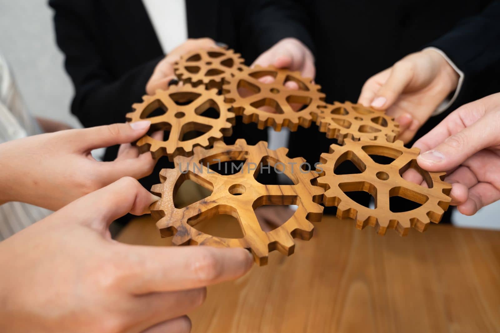 Closeup hand holding wooden gear by businesspeople wearing suit for harmony synergy in office workplace concept. Group of people hand making chain of gears into collective form for unity symbol.