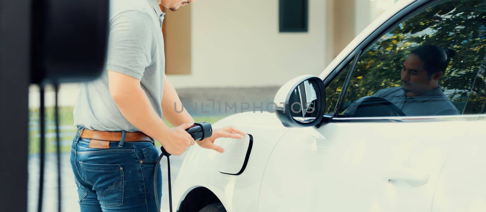 Progressive asian man recharge his EV car at home charging station. by biancoblue