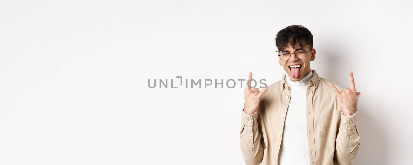 Happy handsome guy showing tongue and rock-on gesture, having fun and feeling upbeat, enjoying something good, standing on white background.