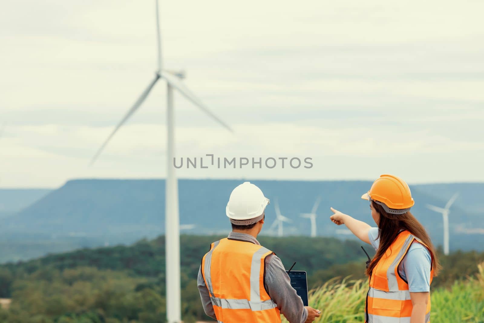 Male and female engineers working on a wind farm atop a hill or mountain in the rural. Progressive ideal for the future production of renewable, sustainable energy.