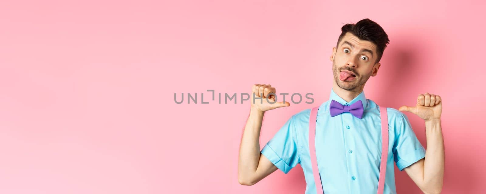 Funny guy in suspenders and bow-tie showing tongue, pointing at himself as if self-promoting, standing over pink background by Benzoix