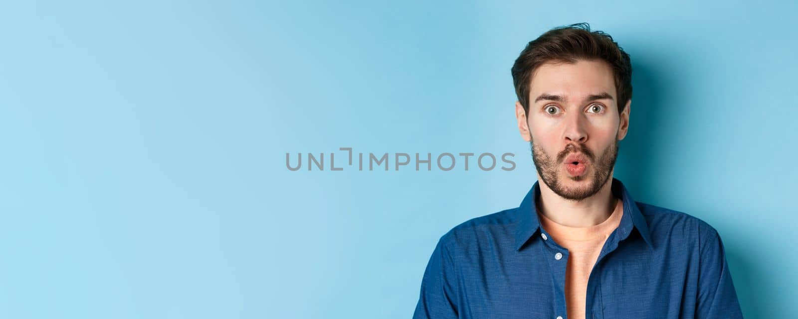 Close up portrait of amazed and surprised man saying wow, staring impressed at camera, checking out cool offer, standing on blue background by Benzoix