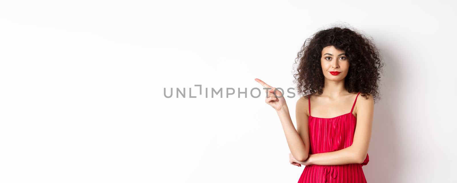 Attractive lady in red dress and makeup pointing finger left, showing logo, standing over white background.