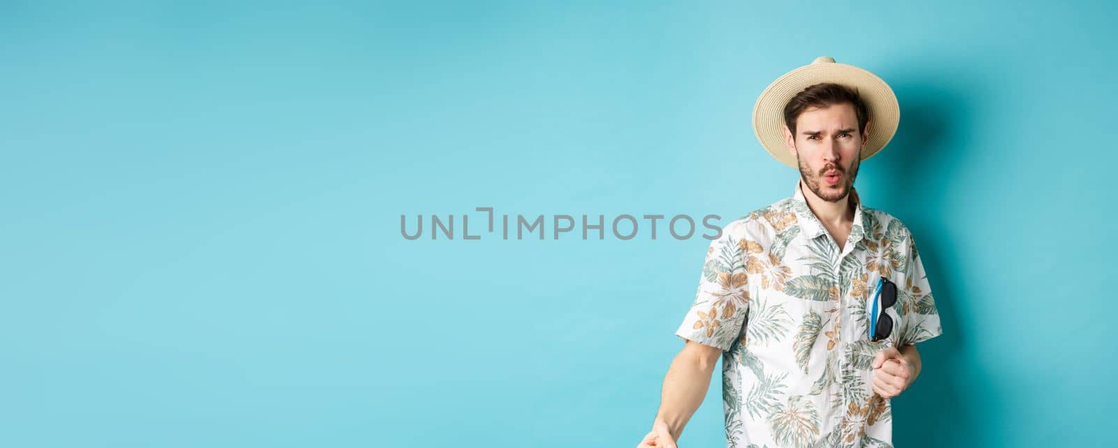 Happy tourist in hawaiian shirt and summer hat dancing, having fun on vacation, standing on blue background by Benzoix