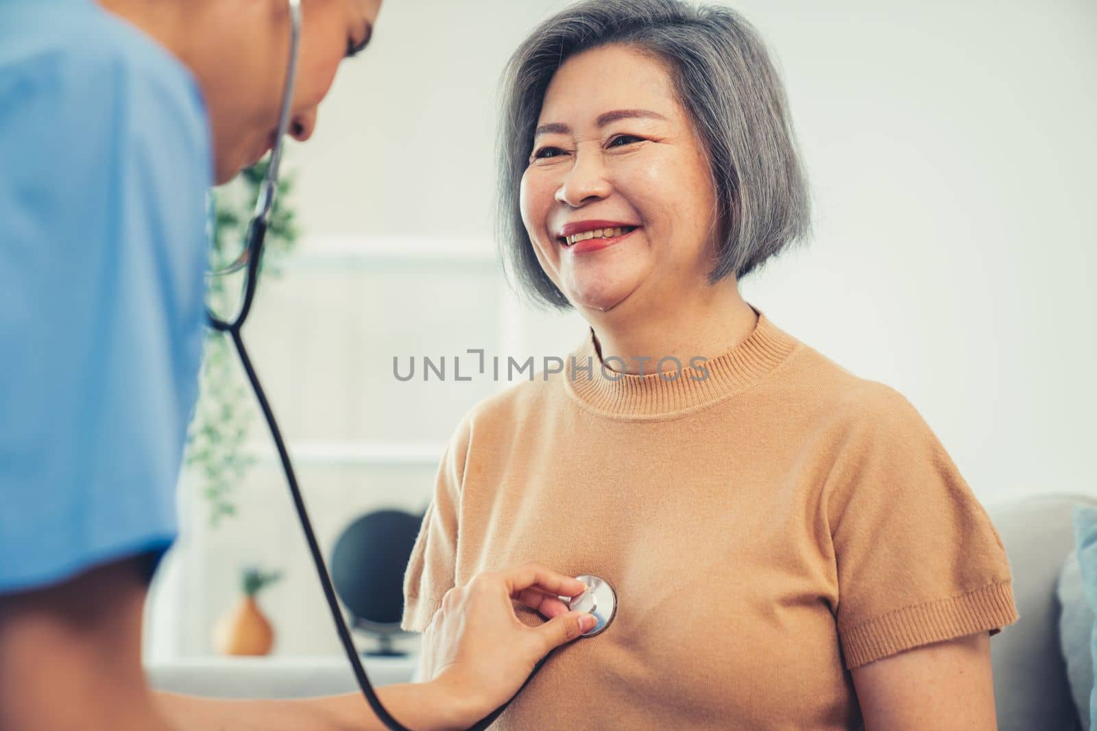 A contented retired senior woman being exterminated by her caregiver with a stethoscope at home. Medical care service, senior care at home.