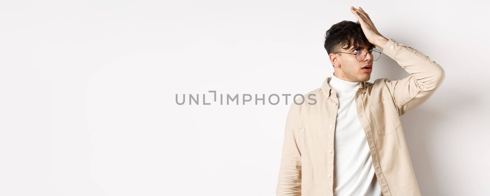 Portrait of annoyed stylish guy facepalm, roll eyes from something stupid, standing on white background tired.