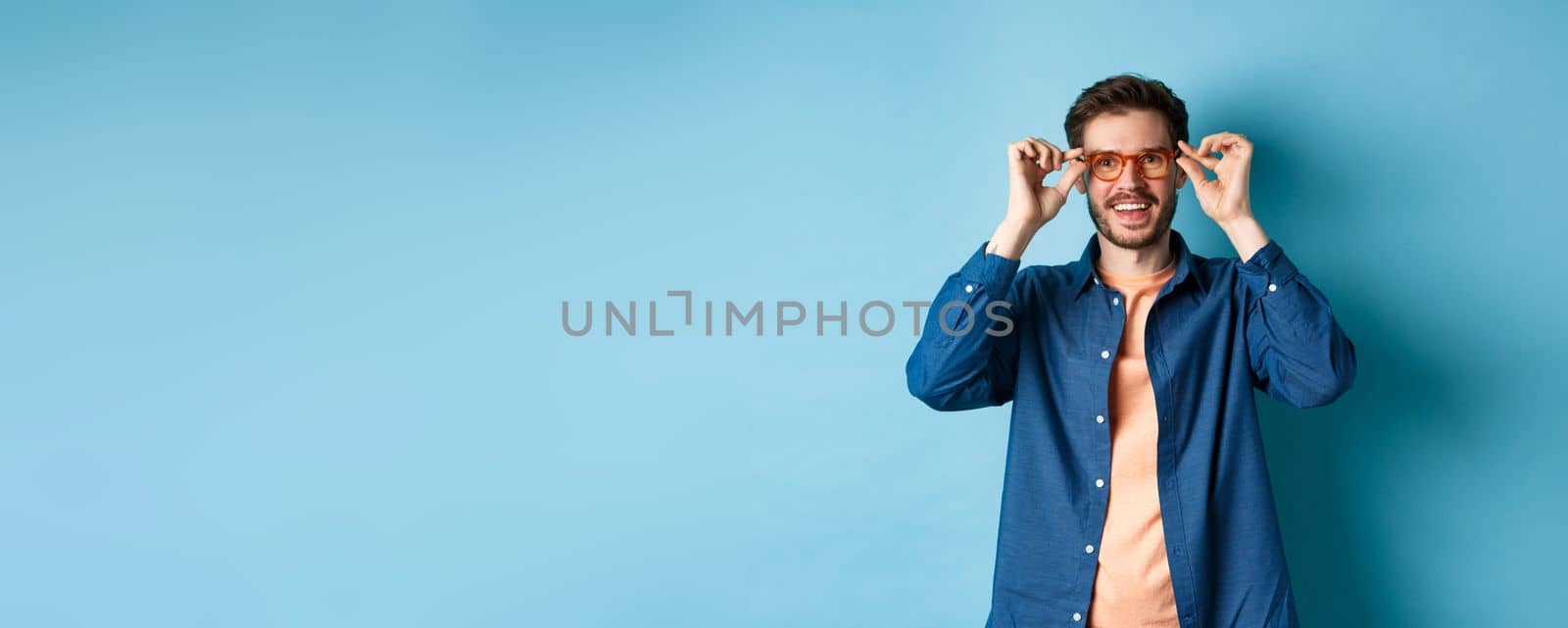 Happy caucasian man trying new glasses and smiling, standing on blue background by Benzoix