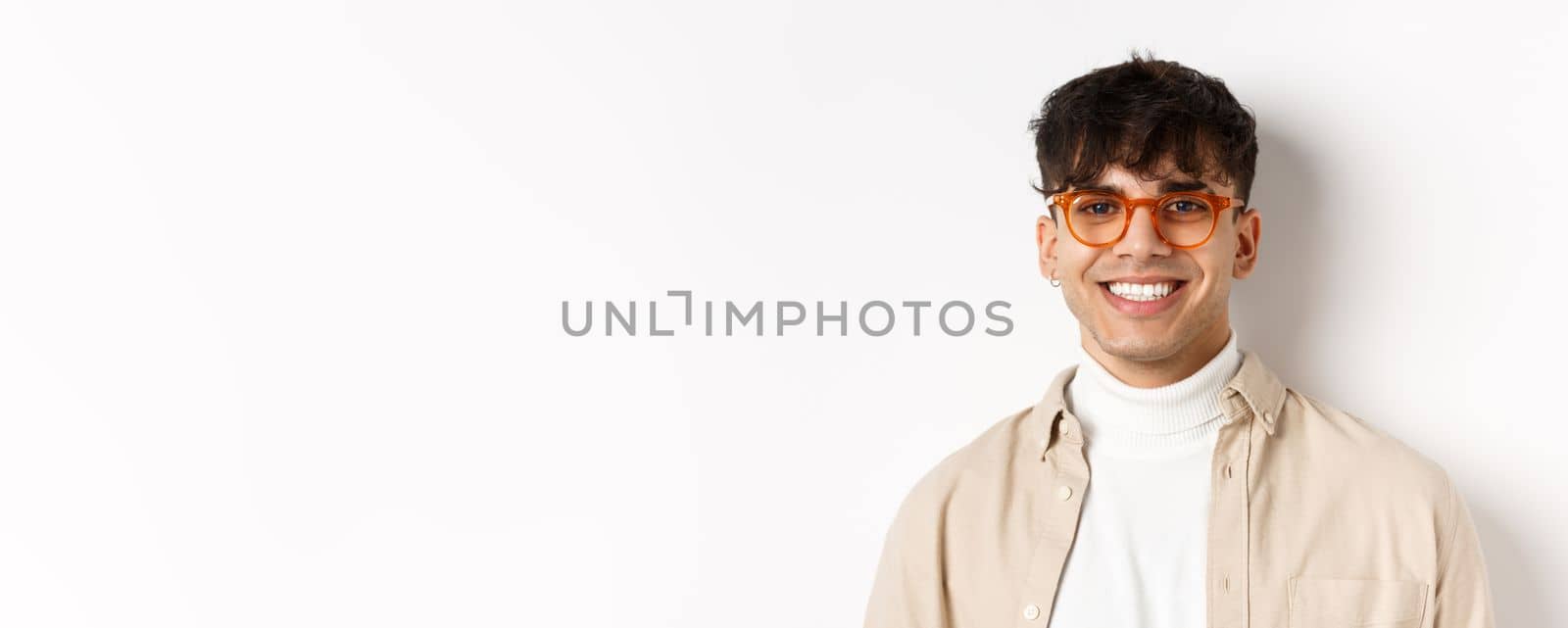 Close-up of handsome hipster guy with natural smile, wearing glasses and earrings, looking happy at camera, standing on white background by Benzoix