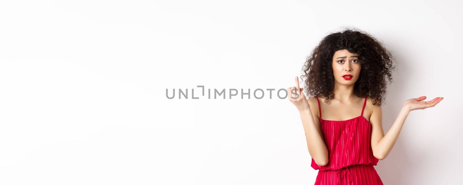 Sad girlfriend with curly hair, showing finger without ring and look confused, complaining at indecisive boyfriend, wanting to get married, standing on white background.