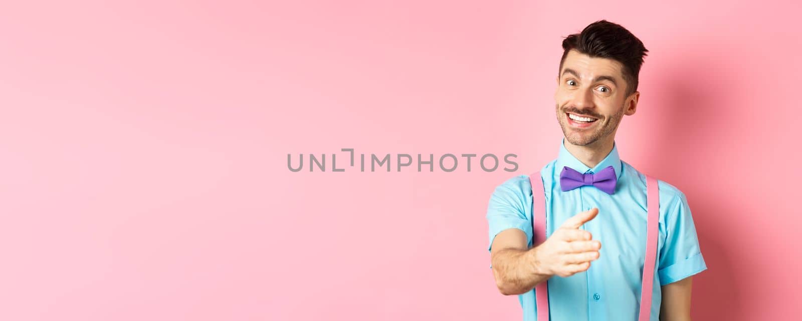 Nice to meet you. Handsome young man stretch out hand for handshake, smiling friendly and polite, introduce himself, standing over pink background by Benzoix