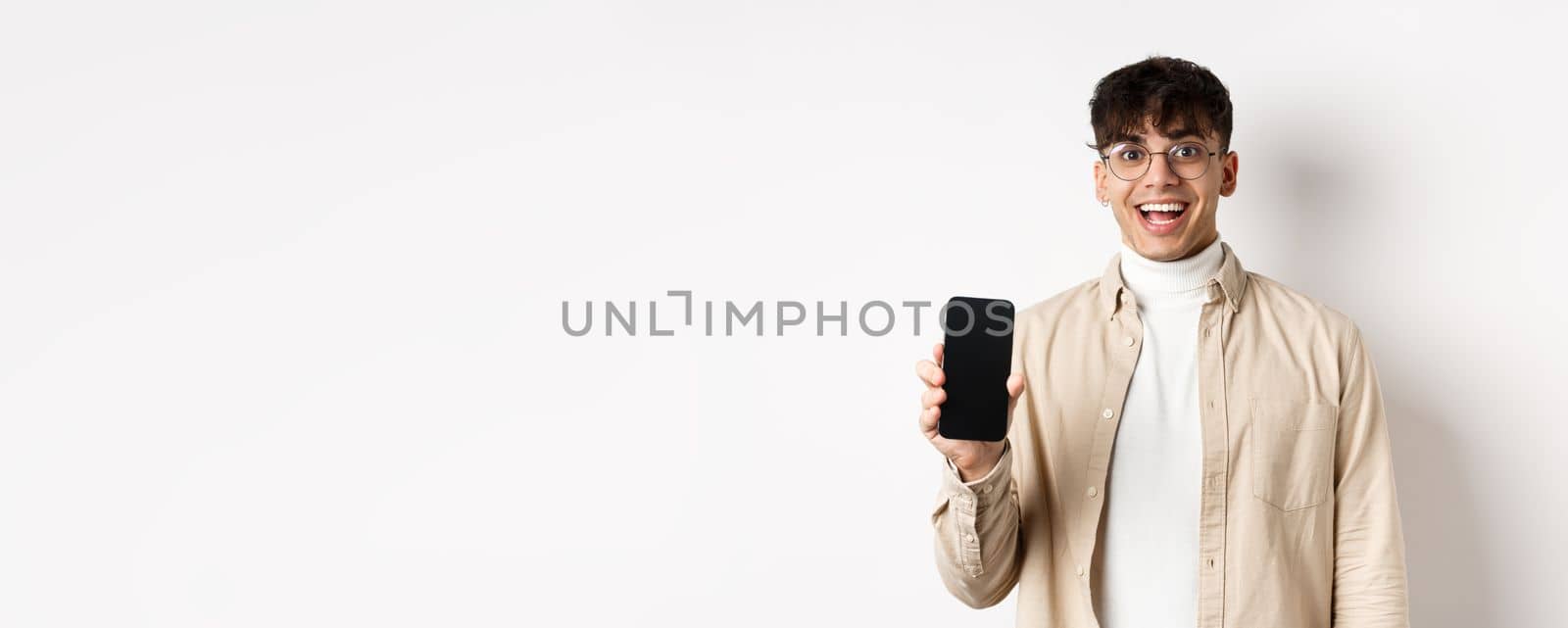 Technology and online shopping concept. Cheerful handsome guy in glasses showing empty smartphone screen and smiling, showing application, standing on white background.