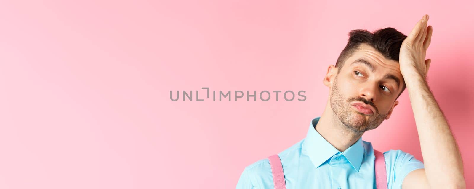 Close-up of handsome caucasian guy with moustache, feeling confident, touching his haircut and looking aside with smug face, standing on pink background by Benzoix