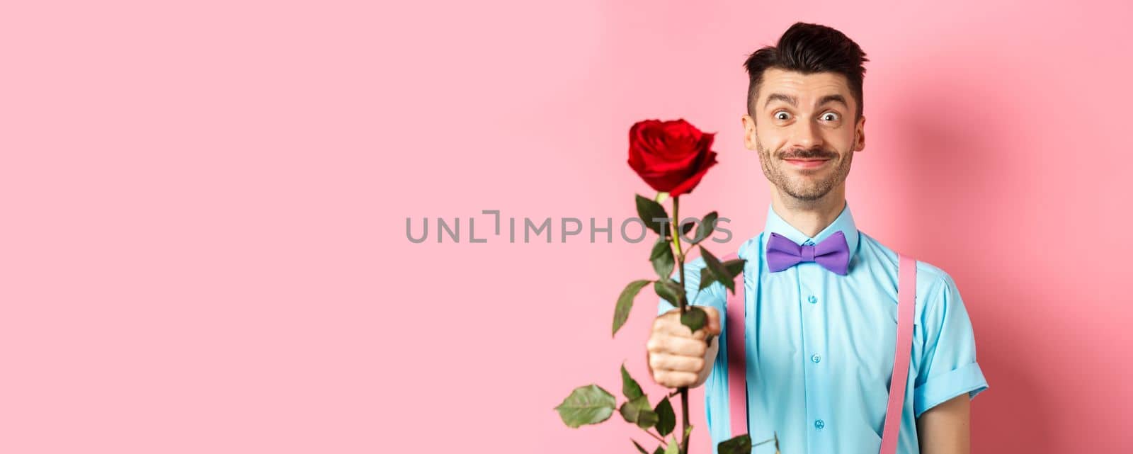 Valentines day and romance concept. Funny guy with moustache giving red rose and smiling, making romantic gesture on date, standing over pink background by Benzoix