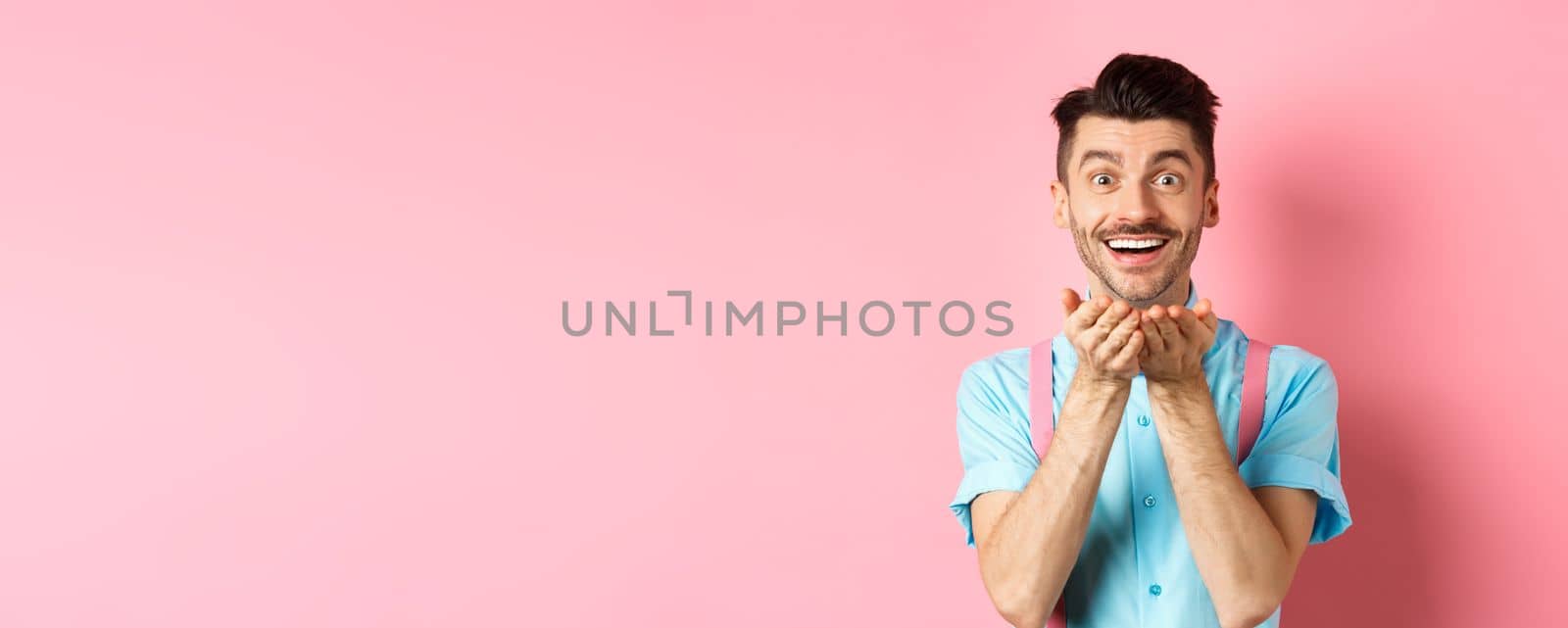 Man in love blowing kiss at camera and smiling passionate, looking at lover happy, enjoying Valentines day, standing over pink background by Benzoix