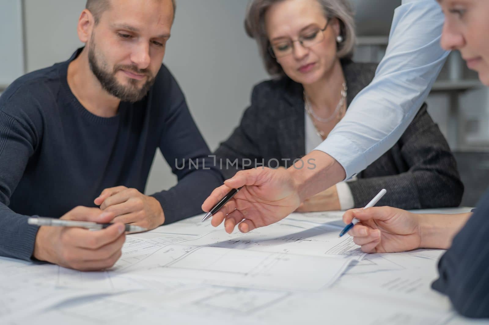 Four colleagues are discussing blueprints in a conference room in an office. Brainstorming of engineers and architects