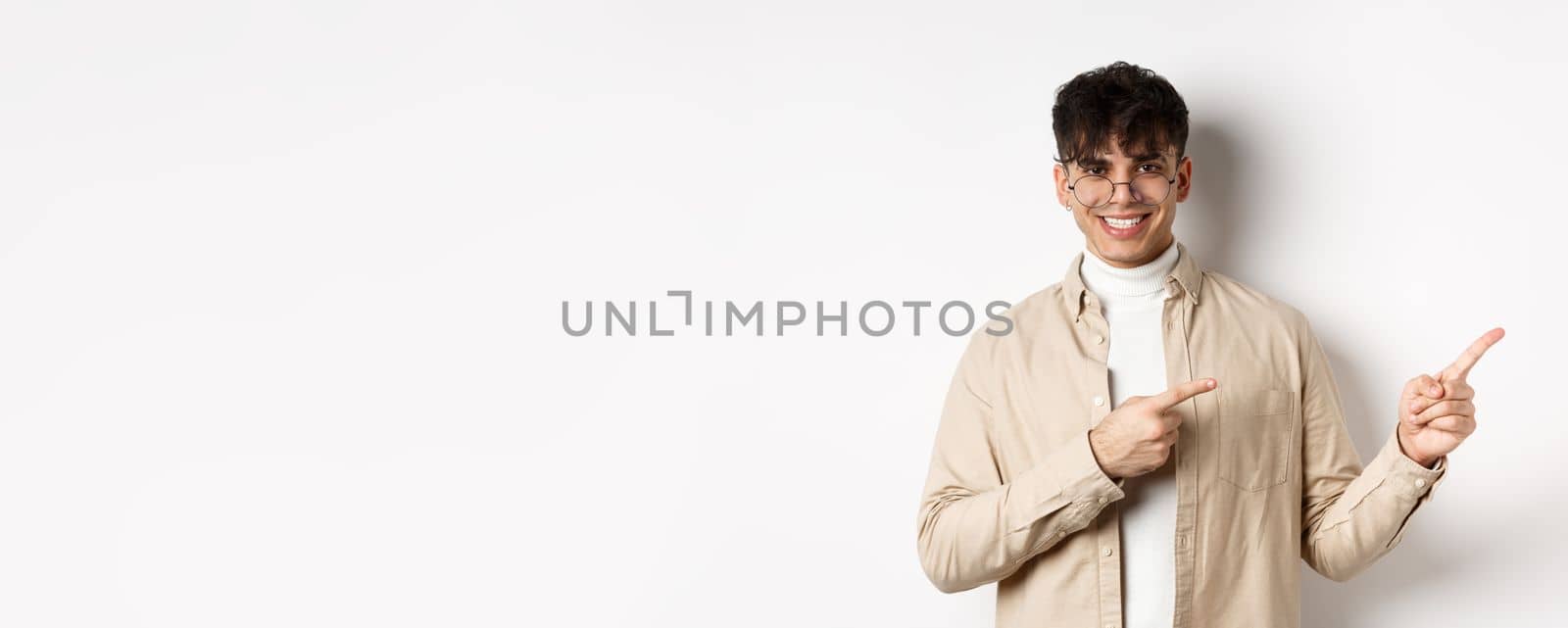 Handsome caucasian man in glasses smiling, pointing fingers at upper right corner, showing logo on white background by Benzoix