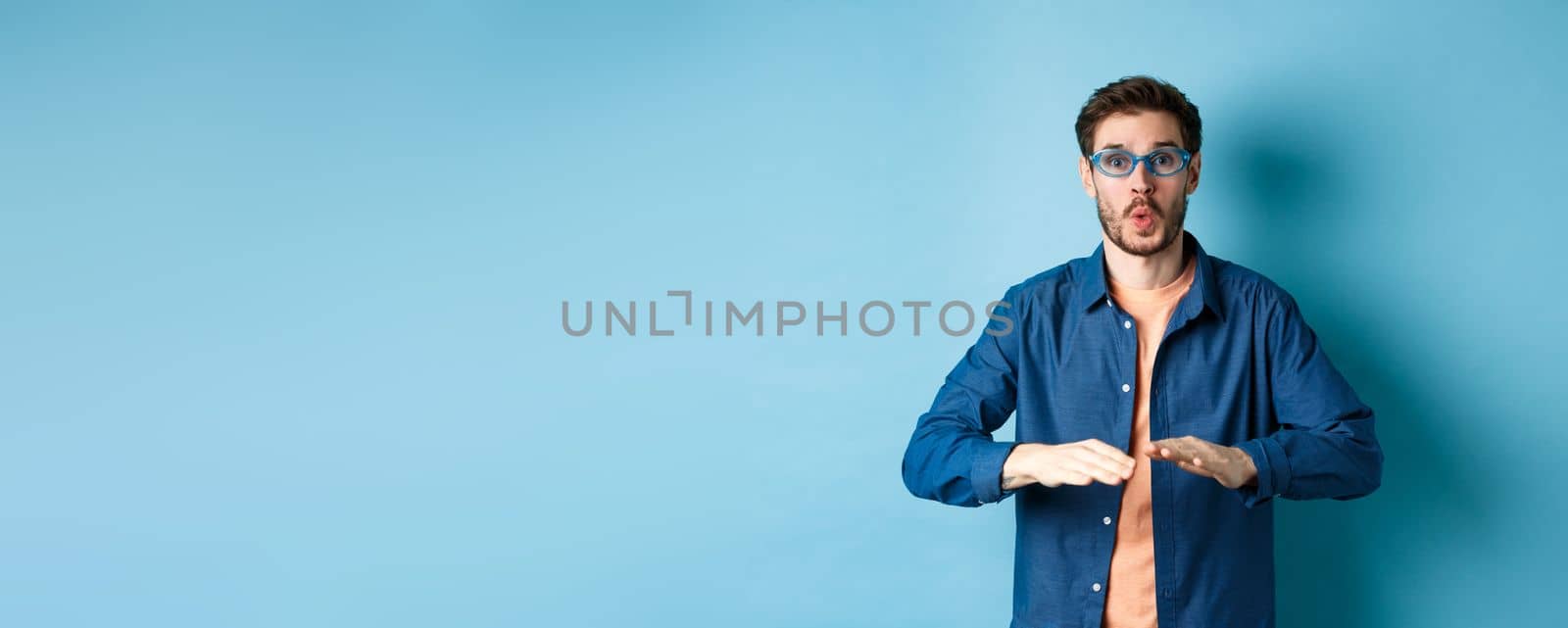 Funny guy trying sunglasses at eyewear store, dancing and having fun, standing on blue background by Benzoix