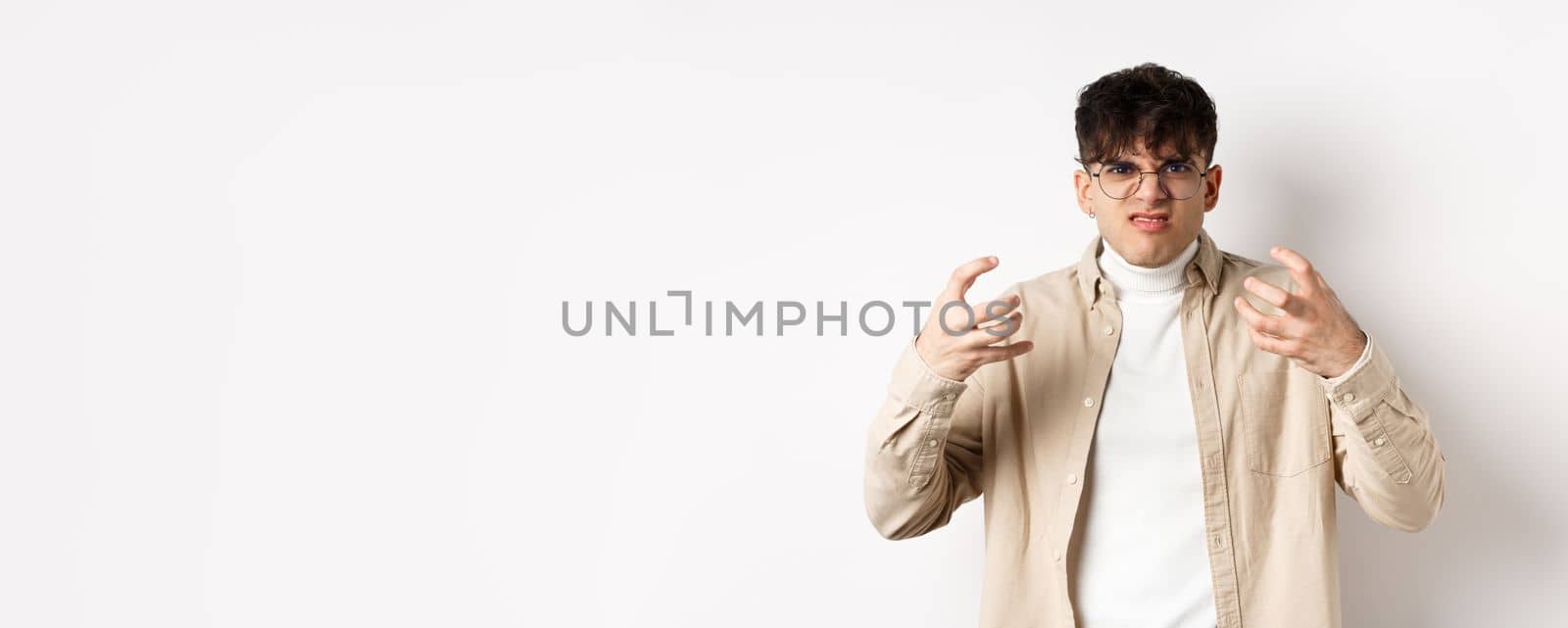 Portrait of annoyed and mad guy wants to strangle someone, grimacing from hatred and clench arms, standing bothered on white background.