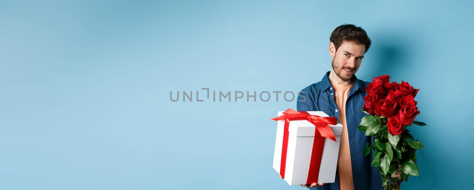 Love and Valentines day concept. Romantic man giving you gift box and bouquet of flowers on date, standing over blue background by Benzoix