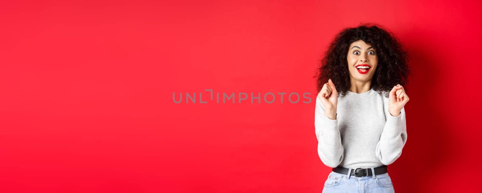 Excited woman winning prize, rejoicing and looking happy, smiling amazed, standing against red background.