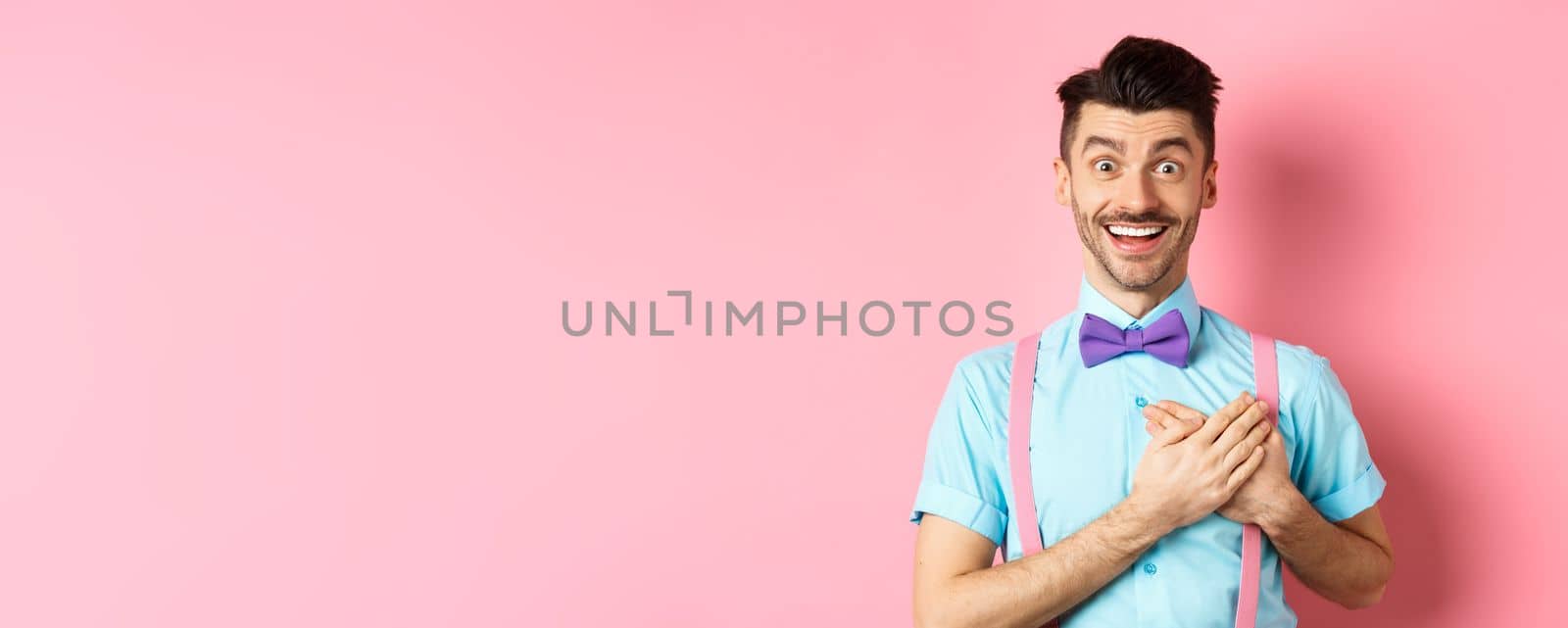 Valentines day and romance concept. Happy man in love holding hands on heart and looking with sympathy at lover, standing on romantic pink background by Benzoix