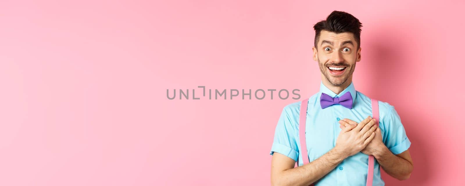 Valentines day and romance concept. Happy man in love holding hands on heart and looking with sympathy at lover, standing on romantic pink background.