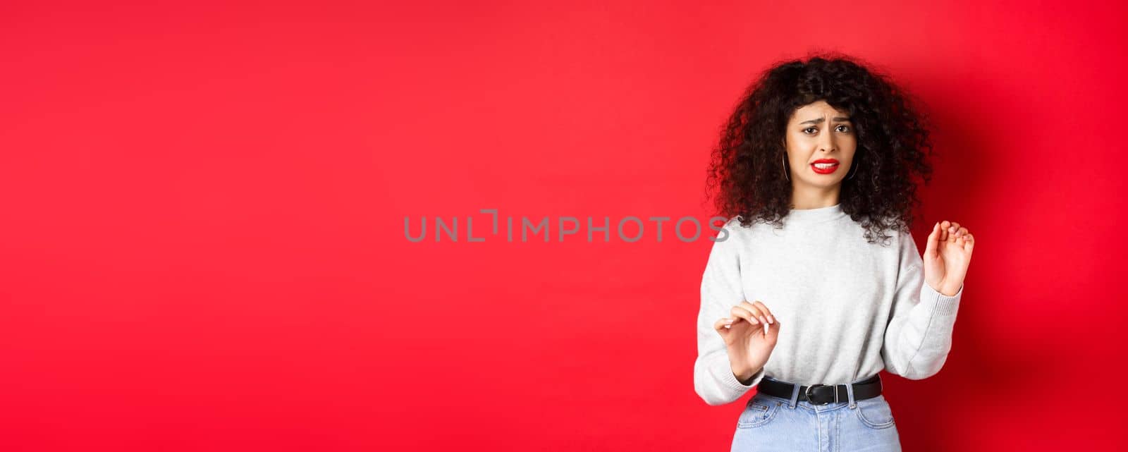 Disgusted and reluctant woman say no, raising hands to block or refuse, asking to stop, looking uncomfortable, standing on red background by Benzoix