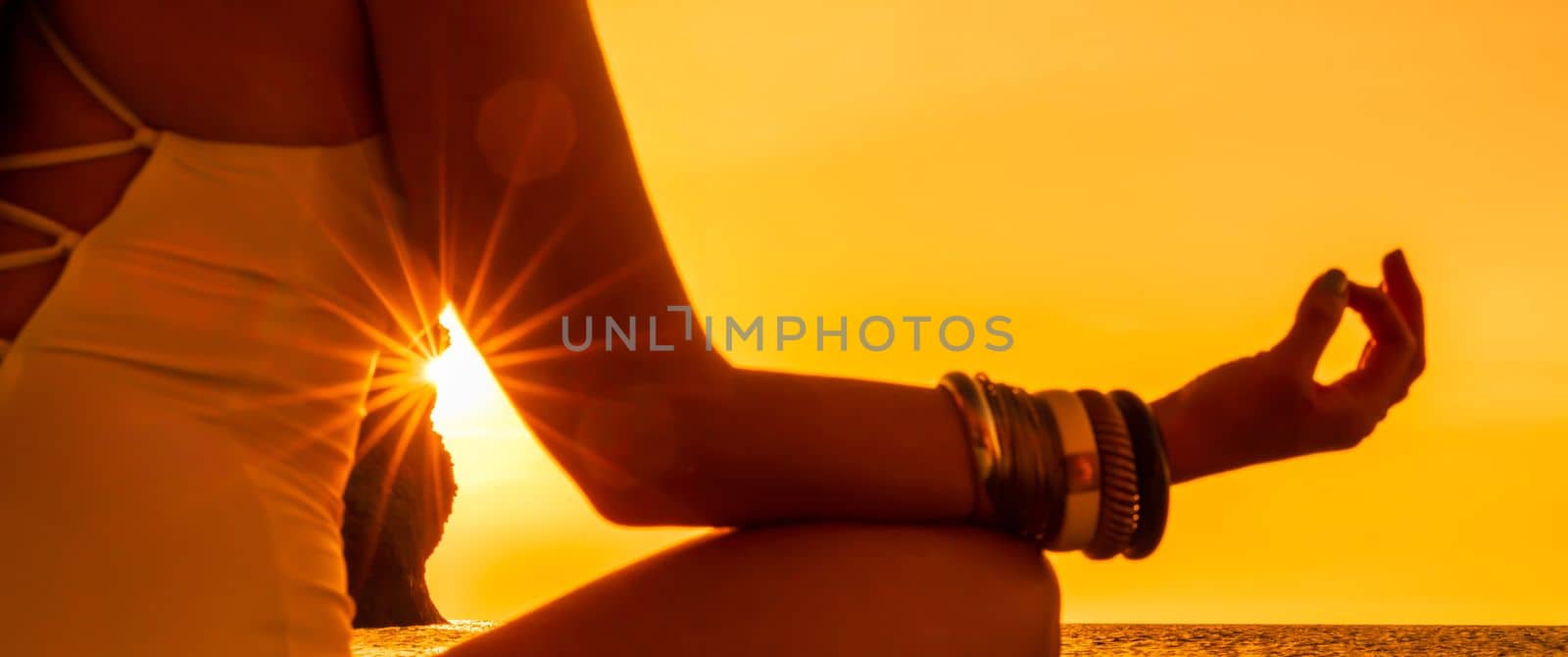 Banner. Young woman practicing yoga on the beach with sunset. Keeps fingers connected, the sun shines through them. The concept of a healthy lifestyle, harmony. by Matiunina