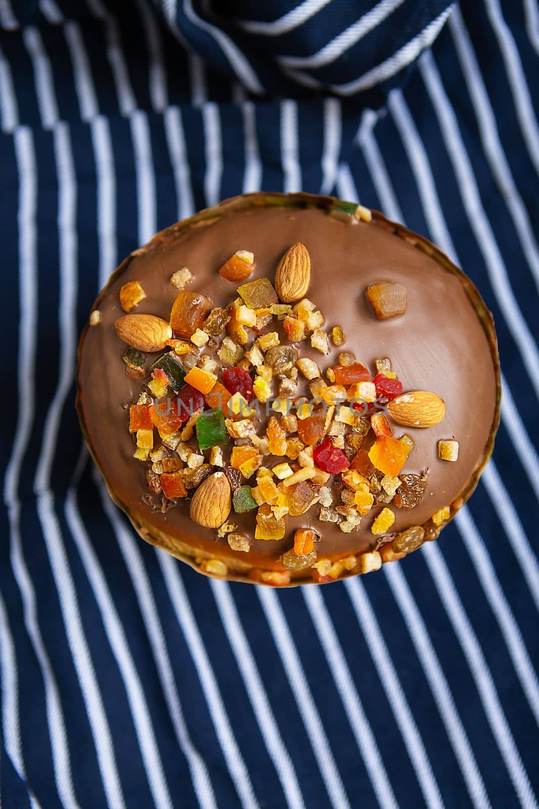 An Easter cake decorated with candied fruits stands on a striped blue apron. Easter religious holiday concept. by sfinks