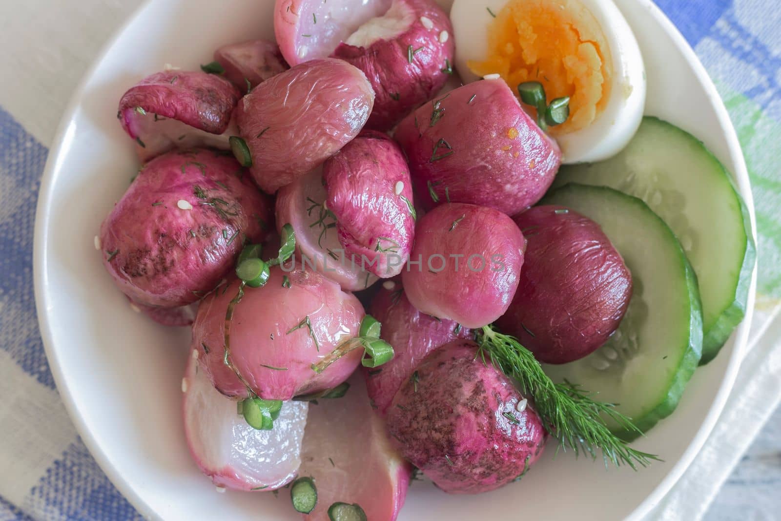 On the table on a plate baked radish with green onions and herbs. Presented in close-up.