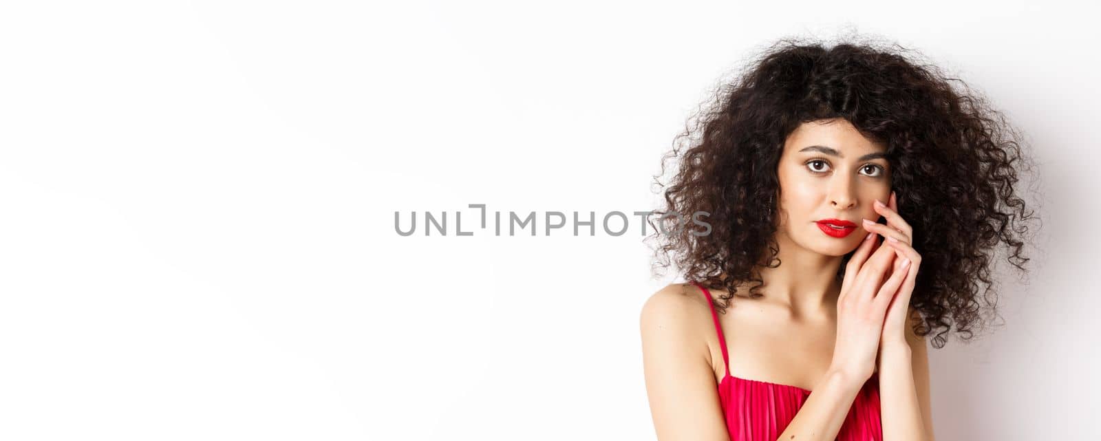 Close-up of tender romantic woman, gently touching face and looking sensual at camera, white background.
