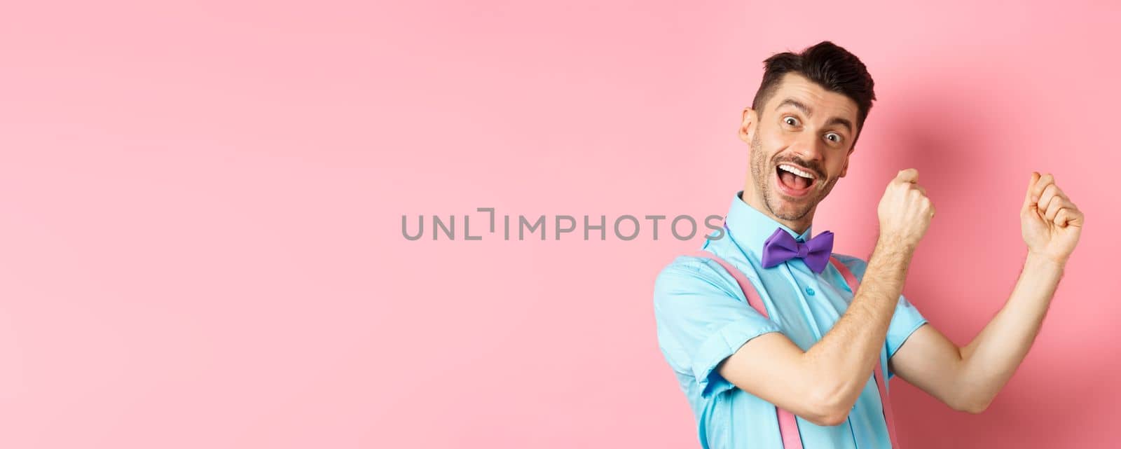 Image of cheerful man celebrating holiday, dancing and having fun, triumphing and saying yes with happy face, standing over pink background.