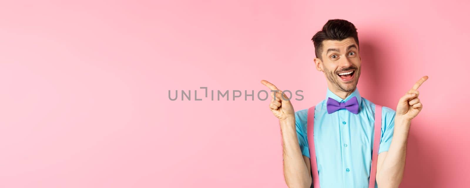 Handsome funny guy pointing fingers aside, showing left and right logo and smiling, recommending two choices, standing on pink background.