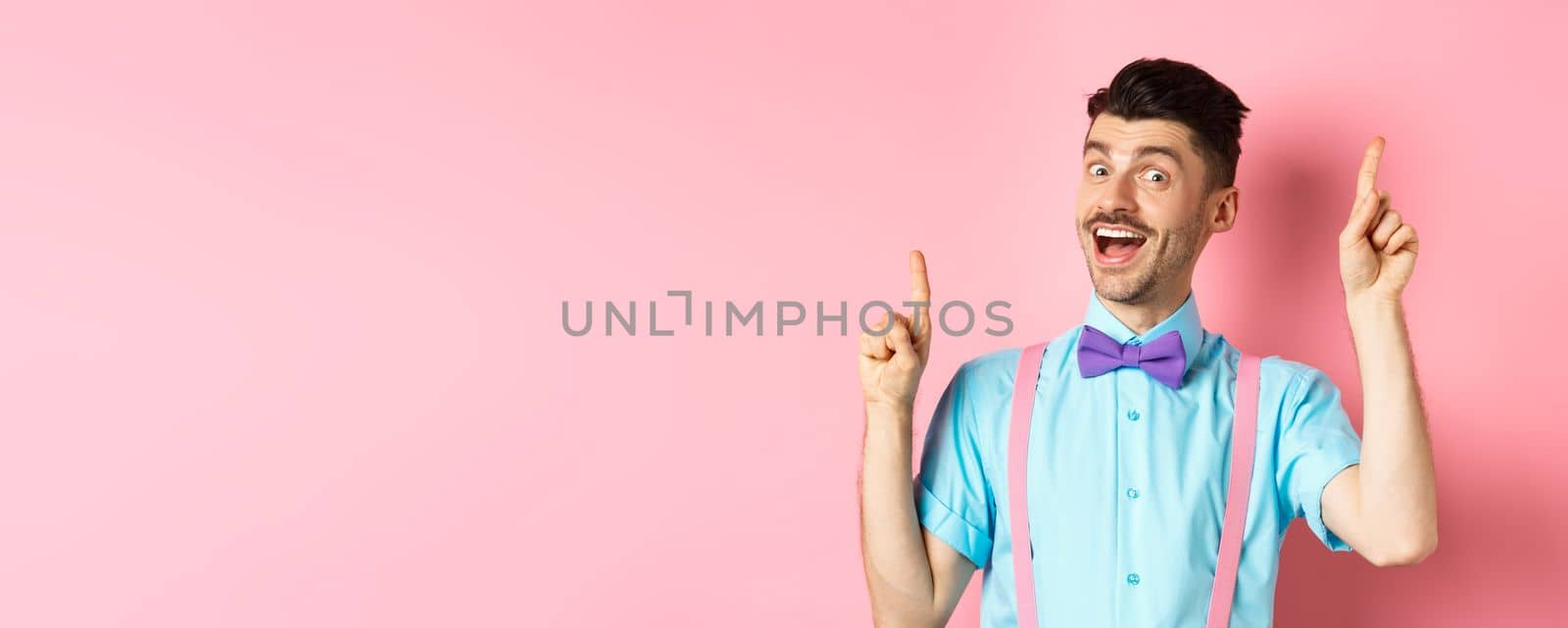 Cheerful guy with french moustache pitching an idea, dancing and raising fingers up, having solution, standing happy over pink background.