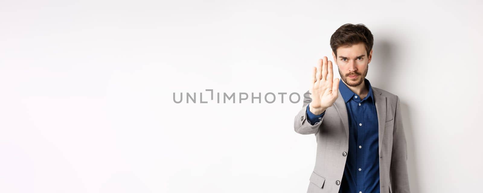 Hold right there. Serious businessman in suit stretch out hand and tell to stop, frowning and look confident, disapprove action, prohibit something bad, standing on white background.