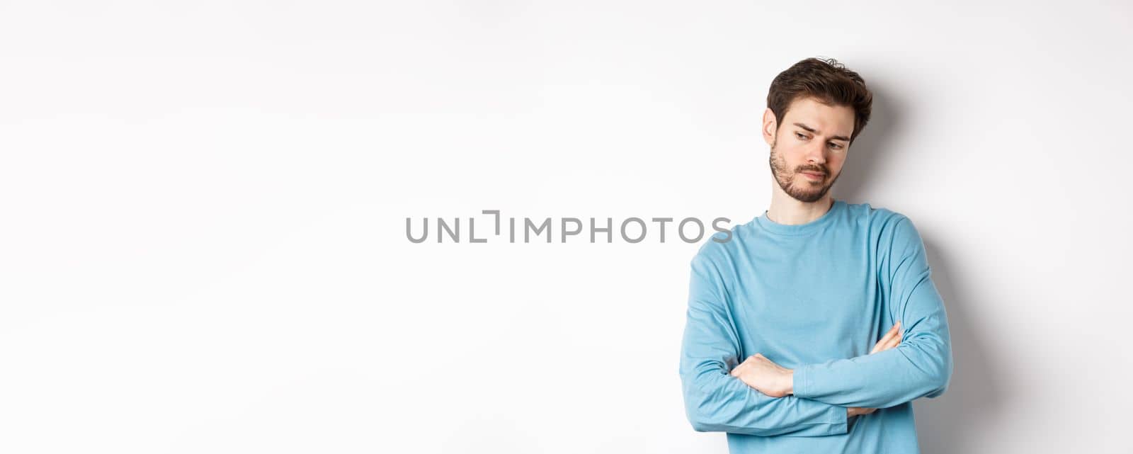 Indecisive and thoughtful bearded man thinking, looking down pensive and making choice, standing over white background by Benzoix