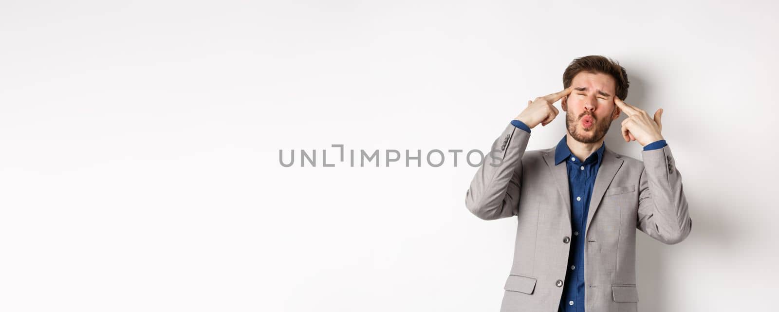 Distressed and tensed businessman pointing at head and complaining, feeling annoyed with situation blowing his mind, standing bothered on white background.