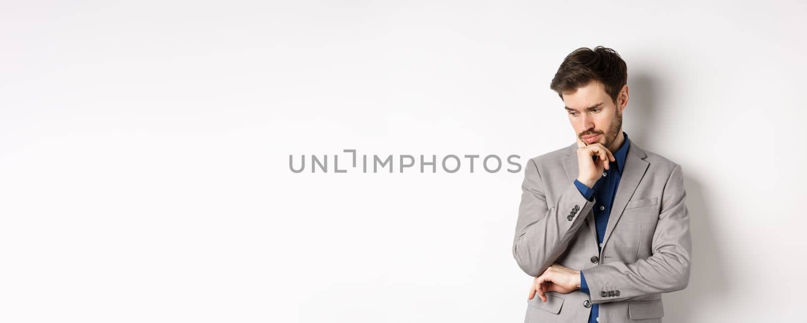 Thoughtful businessman in suit looking down and thinking, making decision, standing on white background.