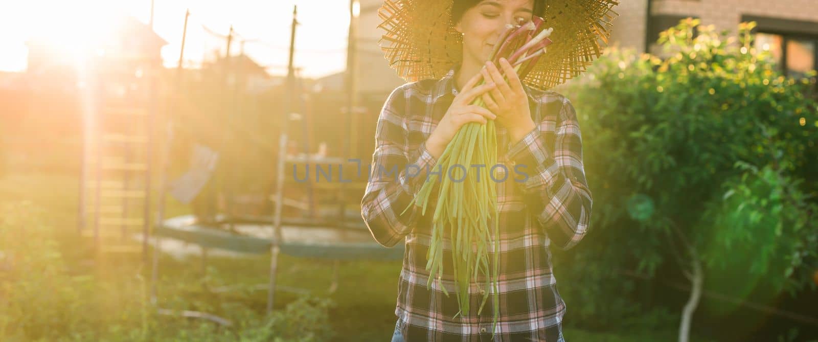 Banner female gardener sniffs bunch of green onions on sunny warm spring day copy space. Plant care and harvest concept and hobby by Satura86
