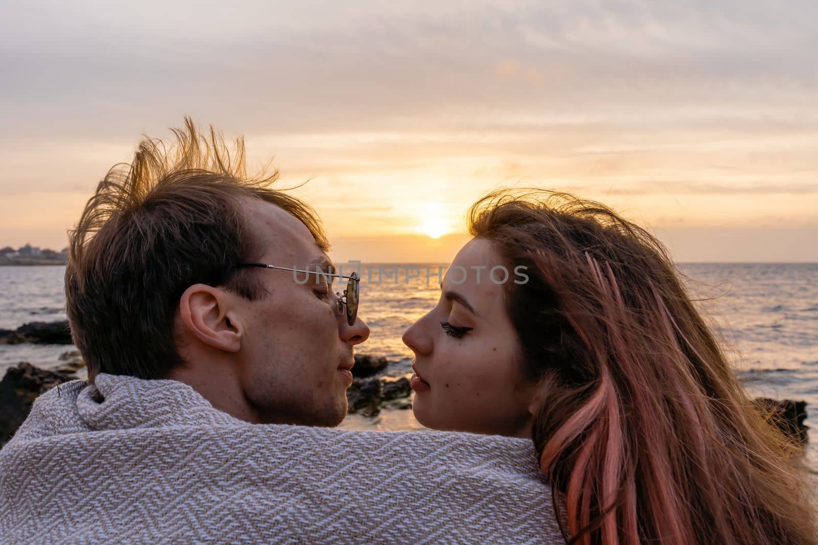 Portraits of lovers, romantic couple of lovers hugging, kissing, touching, eye contact at sunset, sunrise against the background of the sea, sun, clouds in fiery red, orange colors by Matiunina